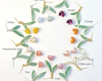 May include: A collection of floral earrings arranged in a circle, featuring translucent petals in yellow, light blue, purple, orange, pearlescent white, pink, glitter pink, and lilac, each with green leaves and a thin metal stem and post backing.