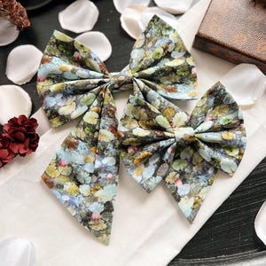 May include: Two fabric bows with a floral pattern in shades of green, blue, and brown. The bows are made of a soft, textured fabric and have a slightly distressed look.