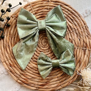 May include: Two green velvet bows with a shimmery finish. The larger bow has long tails, while the smaller bow is a simple, classic shape.