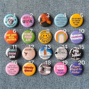 Peut inclure: Une collection de vingt badges ronds disposés en grille, chacun présentant des designs, textes et illustrations colorés uniques, incluant des slogans comme Divine Waters, Keep It Queer, Gay Love Will Prevail et divers autres motifs graphiques.