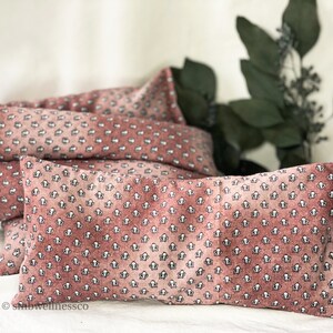 May include: Three pink and white patterned eye pillows with a small floral design. The pillows are stacked on top of each other on a white surface.