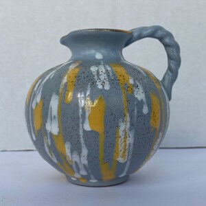 May include: A gray ceramic pitcher with a yellow and white abstract design. The pitcher has a twisted rope handle.