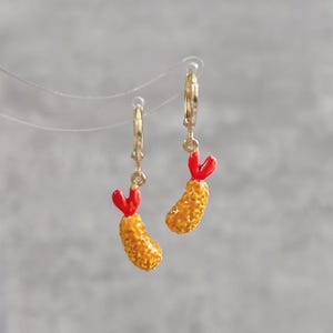 Può includere: Orecchini a cerchio dorati, ciascuno con un ciondolo a forma di gambero tempura. I ciondoli a forma di gambero hanno un corpo marrone dorato strutturato e una coda rossa.