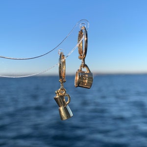 Może przedstawiać: Złote kolczyki koła z wisiorkiem w kształcie dzbanka do kawy i filiżanki. Wisiorki wiszą na kółkach.