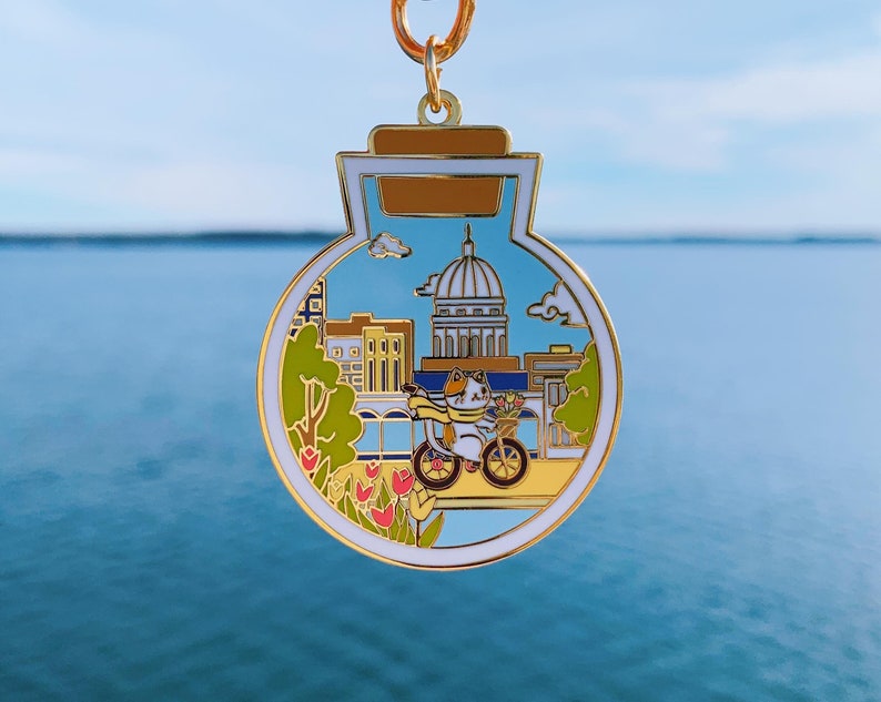 original design of madison w keychain with a cute cat riding bicycle in front of the capitol building