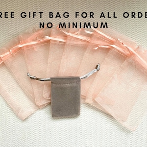Pu&ograve; includere: Un gruppo di 10 piccole buste regalo trasparenti color pesca con una singola busta regalo in velluto marrone al centro. Il testo "FREE GIFT BAG FOR ALL ORDER NO MINIMUM" &egrave; visualizzato sopra le buste.