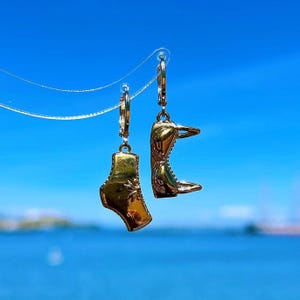 May include: A pair of gold hoop earrings with a gold charm of a bikini top on one earring and a gold charm of bikini bottoms on the other earring.