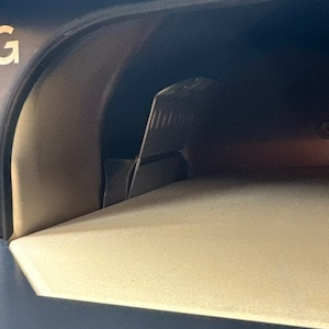 May include: Close-up of the interior of a black pizza oven with a light beige pizza stone inside. The oven door is open and a metal latch is visible.