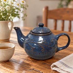 May include: A round, dark blue ceramic teapot featuring a glossy, speckled finish and an embossed vine pattern. The teapot includes a matching lid with a small knob, a curved spout, and a sturdy handle, showcasing a deep blue glaze with brown accents.