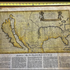 May include: An antique map of North America, featuring California as an island, with text in French and English. The map is aged with yellow and brown tones, and is held in place with clips and a blue clamp. A ruler is at the top.