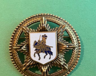 Brass/gold-tone heraldic brooch or badge featuring a central white enamel shield with a knight on horseback