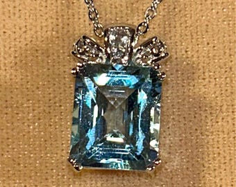 Emerald cut 4.7ctw blue Topaz .925 pendant, topped w/bow w/2 gen wht topaz stones, w/18” ss chain