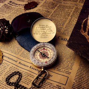 Op de afbeelding: Een gouden kompas met een ketting en een leren etui. Het kompas heeft een wit gezicht met zwarte markeringen en een rode naald. Het etui heeft een inscriptie met de tekst: "Be choose you to be a handful blessings in a hundred smiles, to be a variation of really in any amount, if you really find you need it, choose you. I love you. Christian."