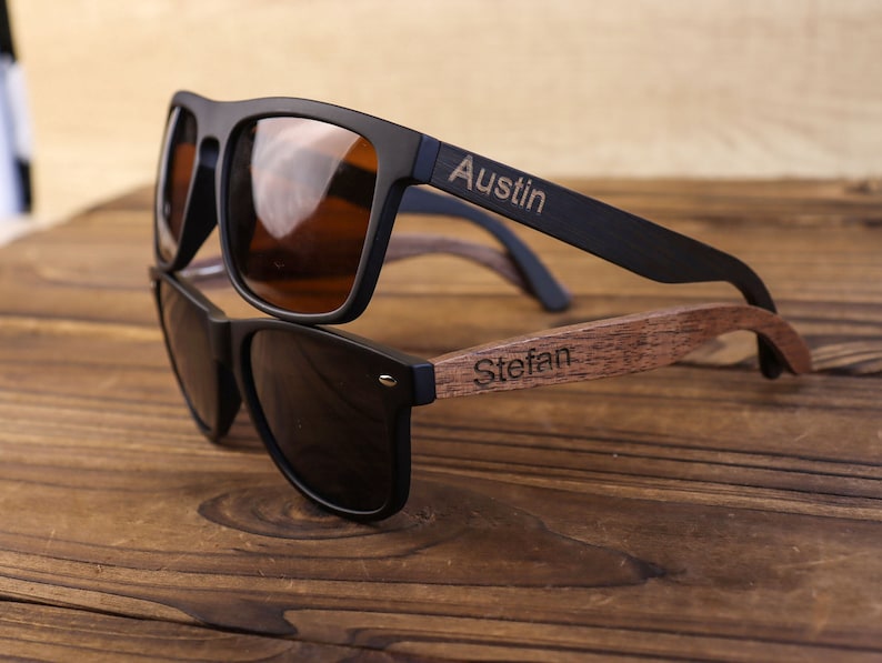 May include: Two pairs of sunglasses with black frames and dark lenses. The top pair has the name "Austin" engraved on the wooden arm. The bottom pair has the name "Stefan" engraved on the wooden arm.