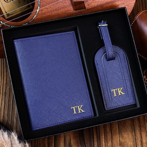 K&ouml;nnte beinhalten: Ein blaues Leder-Reisepass-Etui und ein Gep&auml;ckanh&auml;nger-Set mit goldenen Buchstaben. Das Set ist mit den Initialen "TK" monogrammiert.