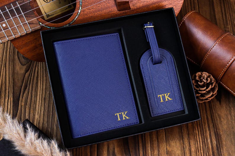 K&ouml;nnte beinhalten: Ein blaues Leder-Reisepass-Etui und ein Gep&auml;ckanh&auml;nger-Set mit goldenen Buchstaben. Das Set ist mit den Initialen "TK" monogrammiert.