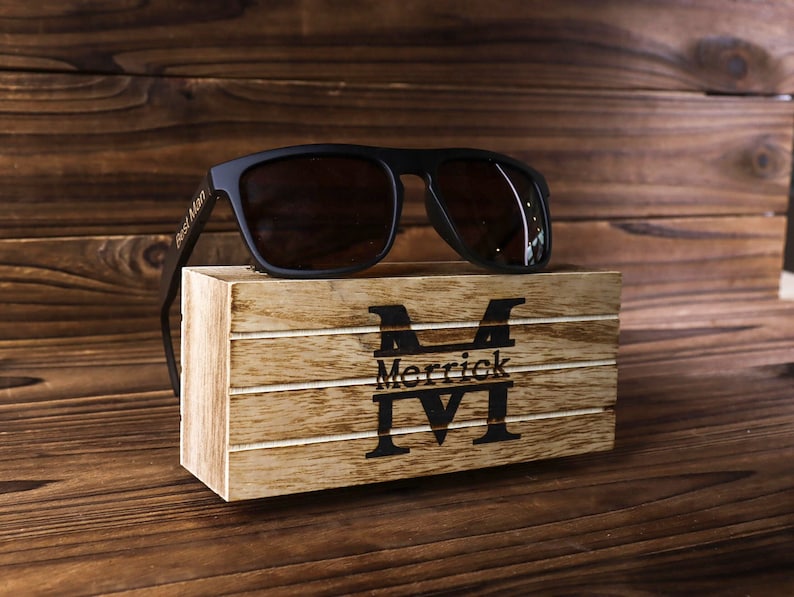 May include: Black sunglasses with a wooden box engraved with the name "Merrick" and the letter "M".