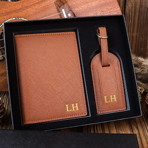 K&ouml;nnte beinhalten: Ein braunes Leder-Reise-Set mit einem Reisepass-Etui und einem Gep&auml;ckanh&auml;nger. Beide Artikel sind mit den Initialen "LH" personalisiert.