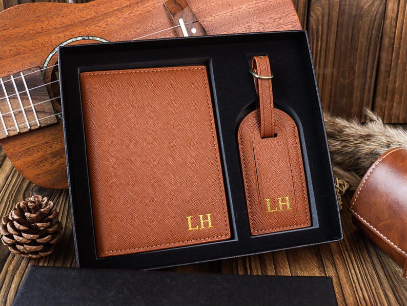K&ouml;nnte beinhalten: Ein braunes Leder-Reise-Set mit einem Reisepass-Etui und einem Gep&auml;ckanh&auml;nger. Beide Artikel sind mit den Initialen "LH" personalisiert.