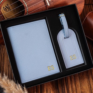K&ouml;nnte beinhalten: Ein blaues Leder-Reisepass-Etui und ein Gep&auml;ckanh&auml;nger-Set mit goldenen Initialen "ES" auf jedem Teil. Das Set wird in einer schwarzen Box pr&auml;sentiert.
