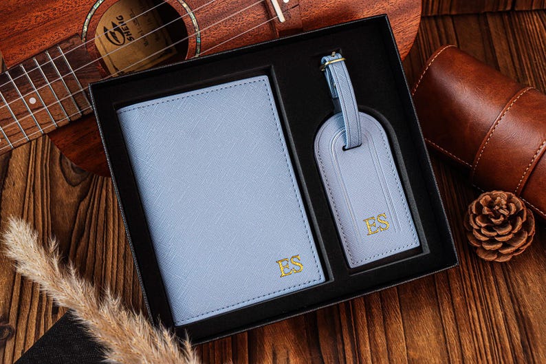 K&ouml;nnte beinhalten: Ein blaues Leder-Reisepass-Etui und ein Gep&auml;ckanh&auml;nger-Set mit goldenen Initialen "ES" auf jedem Teil. Das Set wird in einer schwarzen Box pr&auml;sentiert.