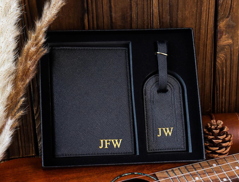 K&ouml;nnte beinhalten: Schwarzes Leder-Reisepass-Etui und Gep&auml;ckanh&auml;nger-Set mit goldener Beschriftung. Das Reisepass-Etui tr&auml;gt die Initialen "JFW" und der Gep&auml;ckanh&auml;nger die Initialen "JW".