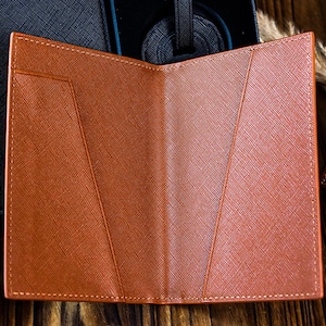 K&ouml;nnte beinhalten: Ein brauner Leder-Reisepass-Etui mit mehreren Kartenf&auml;chern und einem Klappverschluss. Das Etui ist ge&ouml;ffnet und das Innere ist sichtbar.