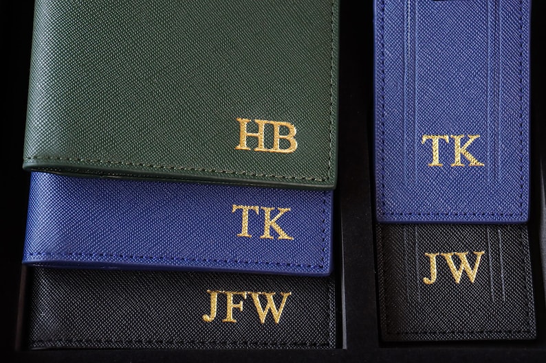 K&ouml;nnte beinhalten: Vier Leder-Gep&auml;ckanh&auml;nger mit goldenen Buchstaben. Die Anh&auml;nger sind in verschiedenen Farben: gr&uuml;n, blau, schwarz und dunkelblau. Die Initialen auf den Anh&auml;ngern sind HB, TK, JFW und JW.