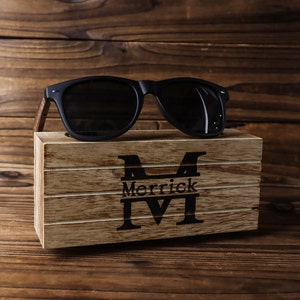 May include: A wooden box with a personalised inscription "Merrick M" and a pair of black sunglasses on top.