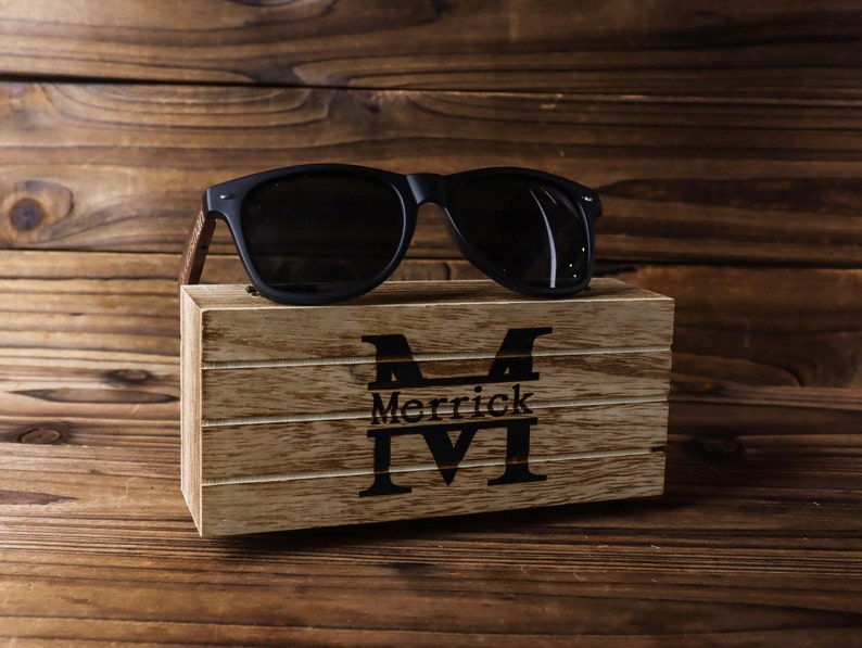 May include: A wooden box with a personalised inscription "Merrick M" and a pair of black sunglasses on top.
