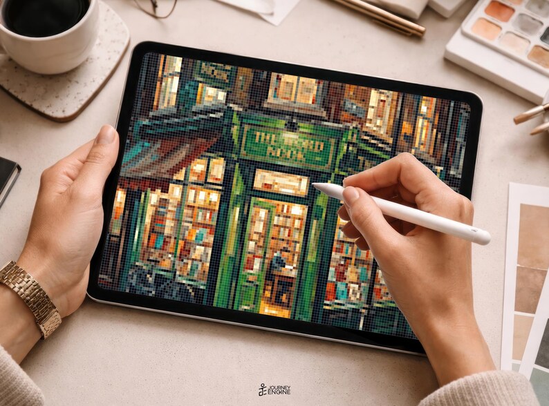 May include: A digital tablet displaying a pixel art illustration of a green storefront with the text THE BOOK NOOK visible above the entrance. The artwork features warm interior lighting, shelves filled with books, and a detailed facade design.
