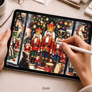 May include: A digital tablet displaying a pixelated illustration of three nutcracker figures in red, gold, and blue uniforms. The screen shows a detailed grid-based design with festive colors, while a white stylus is held against the display surface.