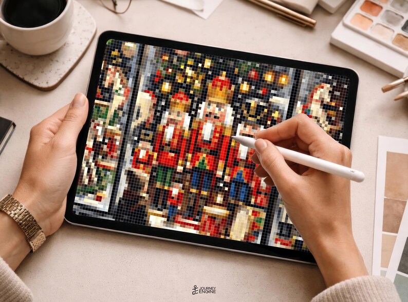 May include: A digital tablet displaying a pixelated illustration of three nutcracker figures in red, gold, and blue uniforms. The screen shows a detailed grid-based design with festive colors, while a white stylus is held against the display surface.