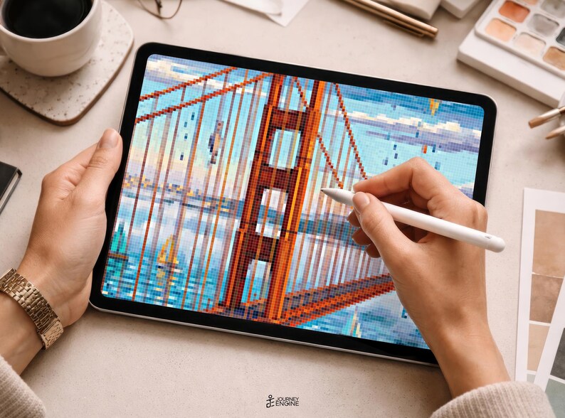May include: A tablet displaying a pixelated digital illustration of the Golden Gate Bridge in orange, set against a blue sky and water background. A white stylus is held against the screen, which also features the text Journey Engine at the bottom.