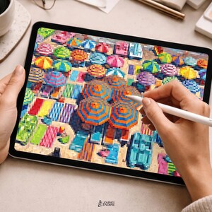 May include: A digital tablet displaying a pixel art illustration of a crowded beach scene with numerous colorful umbrellas and beach towels. The screen shows a high-angle view of the sand filled with vibrant geometric patterns and shapes.