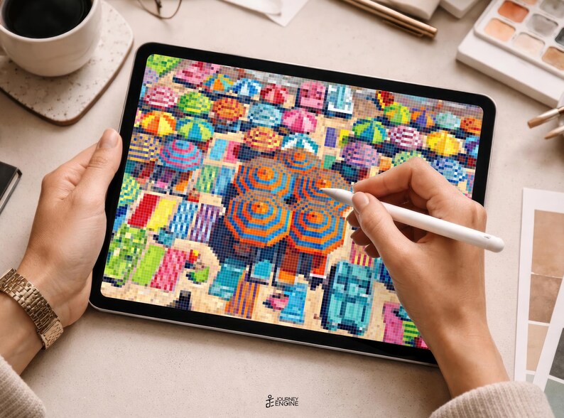 May include: A digital tablet displaying a pixel art illustration of a crowded beach scene with numerous colorful umbrellas and beach towels. The screen shows a high-angle view of the sand filled with vibrant geometric patterns and shapes.