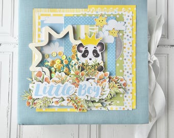 May include: A blue scrapbook with a panda bear wearing a crown and surrounded by yellow and green flowers. The scrapbook has the words "Little Boy" on the front.