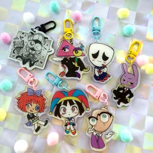 May include: A collection of colorful acrylic keychains featuring various cartoon characters. Each keychain has a unique design, including a cat, a triangle-headed figure, a character in a sailor uniform, and a purple rabbit. The keychains are attached to metal clasps.