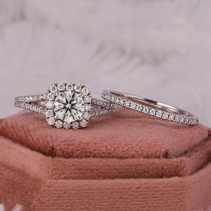 May include: A square halo engagement ring set with a center stone and a matching wedding band. Both rings are set with sparkling diamonds.