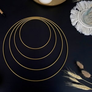 Könnte beinhalten: Vier goldene Metallreifen in verschiedenen Größen, die konzentrisch auf einem schwarzen Hintergrund angeordnet sind. Außerdem sind eine Rolle gelber Garn und eine goldene Schere zu sehen.