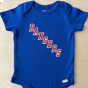 May include: A blue baby onesie with the word "RANGERS" in red letters on the front. The onesie is made by Gerber and has the onesies logo on the bottom.