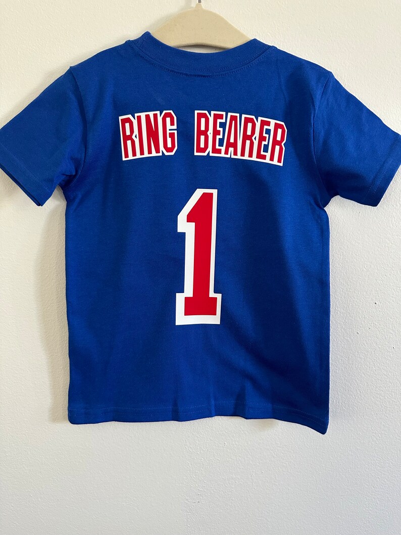 May include: A blue t-shirt with the words "Ring Bearer" and the number "1" in red and white lettering on the back.