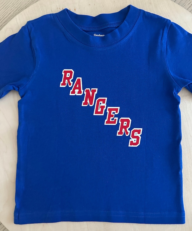 May include: A blue long-sleeved t-shirt with the word "RANGERS" in red letters with white outlines.