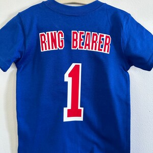May include: Blue t-shirt with the words "Ring Bearer" and the number "1" in red and white on the back.