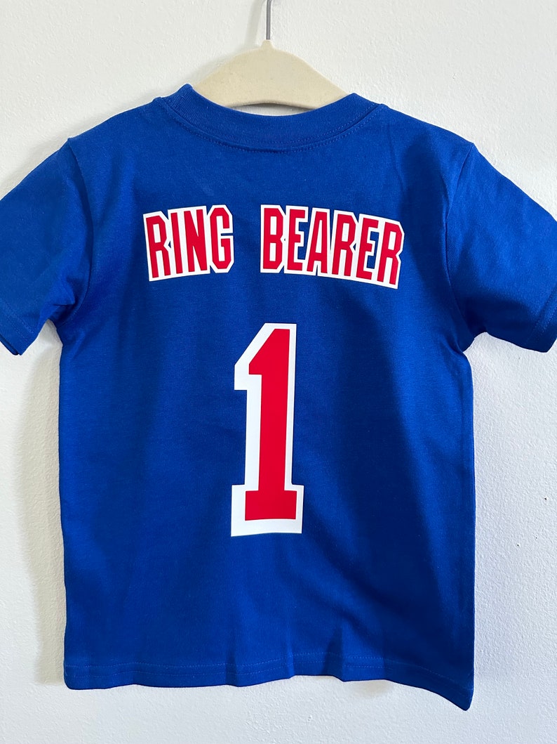 May include: Blue t-shirt with the words "Ring Bearer" and the number "1" in red and white on the back.