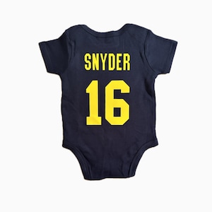 May include: A navy blue baby onesie with the name "SNYDER" and the number "16" printed in yellow on the back.