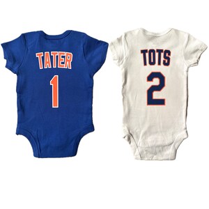 May include: Two white and blue baby onesies with the names "Tater" and "Tots" and the numbers 1 and 2 on the back.