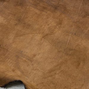 Puede incluir: Primer plano de un trozo de cuero marr&oacute;n con una superficie texturizada. El cuero tiene un aspecto natural e irregular con variaciones de color y tono. Los bordes del cuero son visibles.