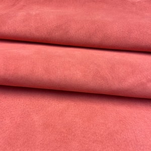 Può includere: Primo piano di un morbido tessuto in pelle scamosciata rosa. Il tessuto è piegato in diversi punti, mostrando la trama e il colore.