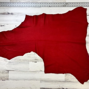 May include: A large piece of red leather, measuring 6.3 square feet, is laid out on a white wooden surface. The leather has a smooth, even texture and is a rich, deep red color.